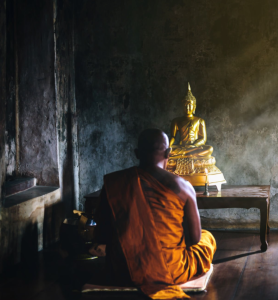 Monk in front of a golden Buddha, Laos